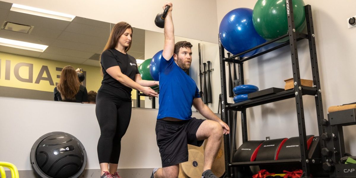 person exercising with weights in presence of a trainer